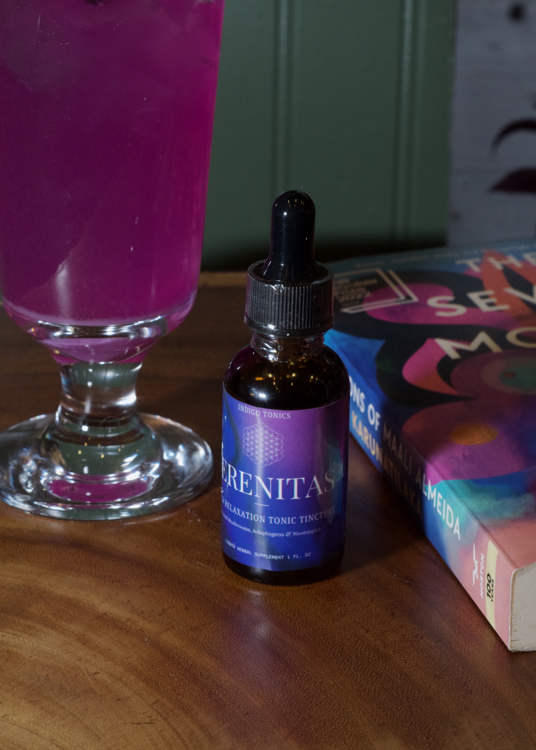 Serenitas relaxation tonic tincture bottle, styled with a cocktail and books